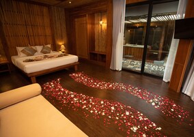 Een slaapkamer met een bed, houten wanden, een glazen deur die uitkomt op een balkon en een vloer bedekt met rozenblaadjes.