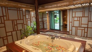 Un área de spa con una bañera grande llena de agua y pétalos de rosa, rodeada de piso de madera y techo de bambú.