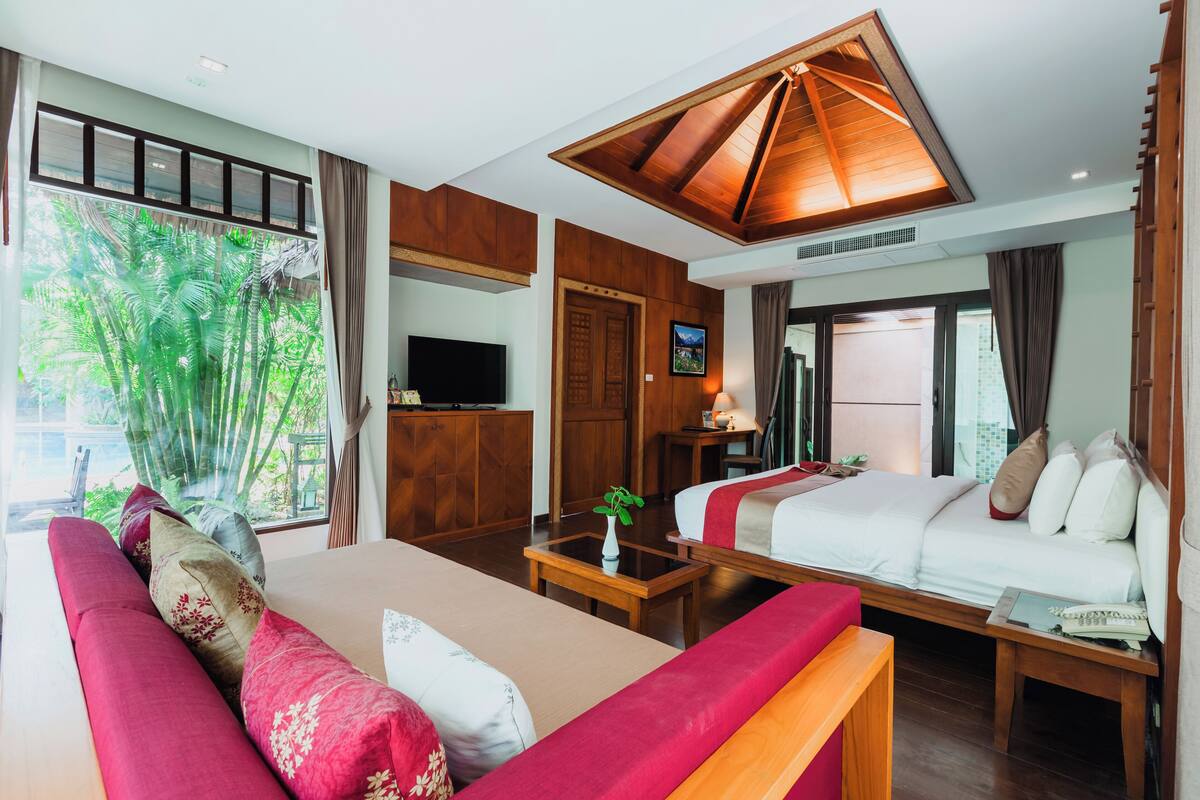 A modern hotel room with a large bed, a sofa, a TV, and a wooden ceiling.