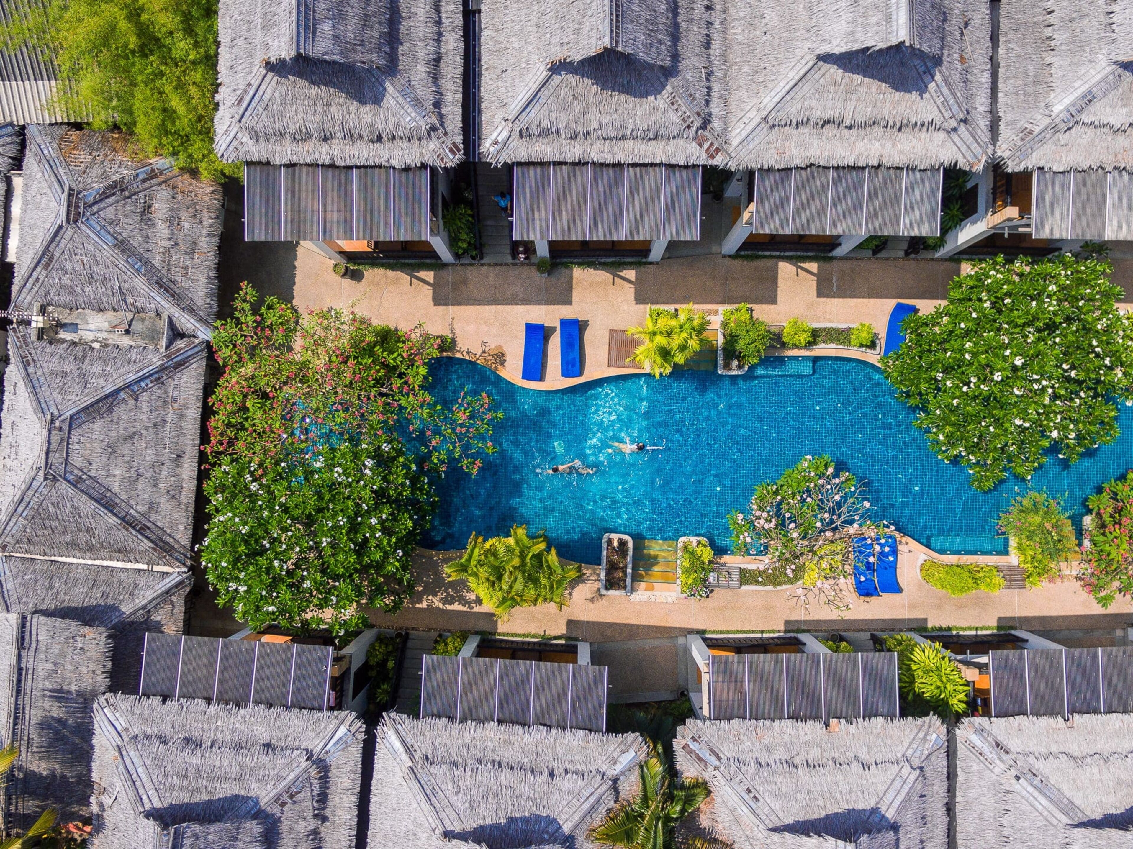 An aerial view of a resort with multiple thatched-roof bungalows surrounding a central swimming pool.