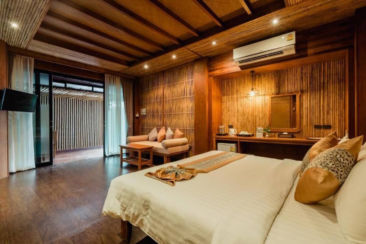 A spacious bedroom with a large bed, a sitting area with a sofa and table, and a wooden wall paneling.