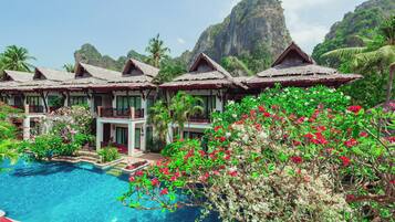 Een resort met bungalows met rieten daken, een zwembad en weelderige tropische begroeiing.