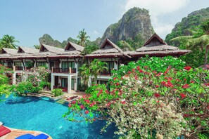 Un resort con bungalós de techo de paja, piscina y exuberante vegetación tropical.