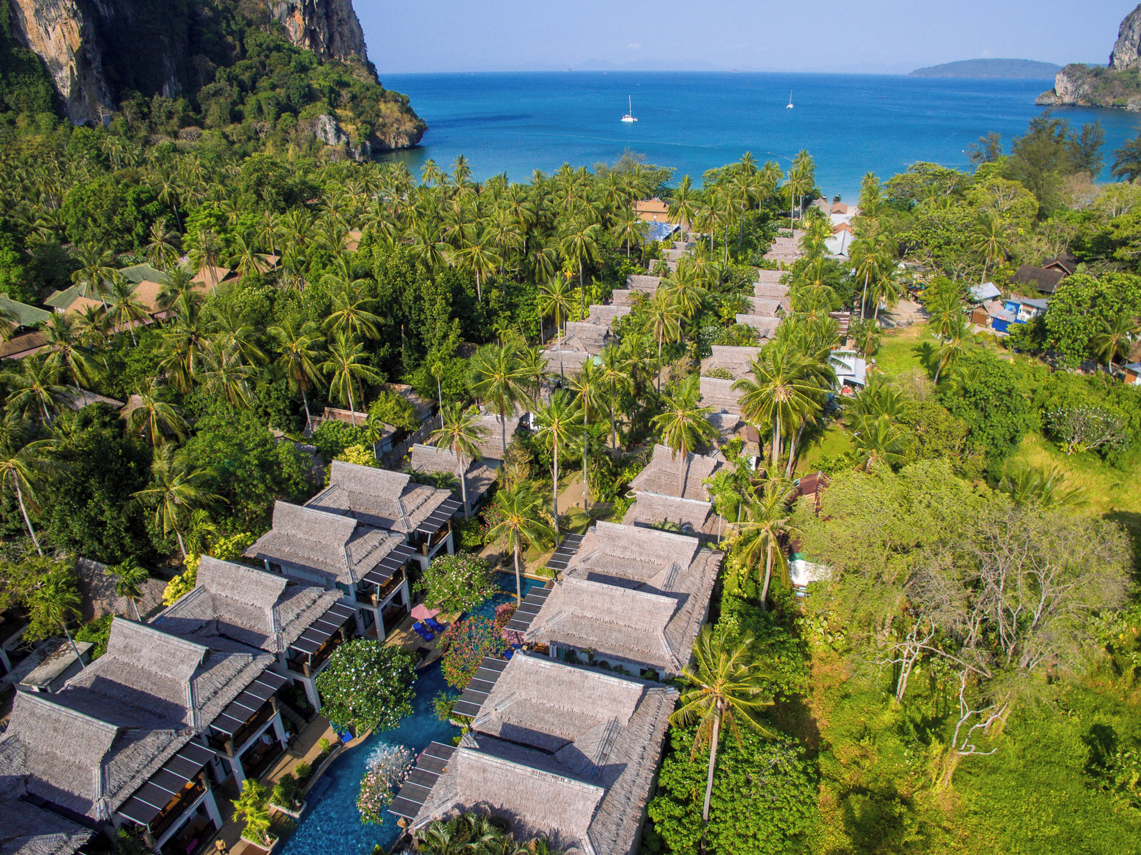Vista aérea de un resort con bungalows de techo de paja, una piscina y vistas al océano.