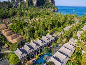 Vista aérea de un complejo turístico con bungalows sobre el agua, una piscina y vistas al océano y a los acantilados.