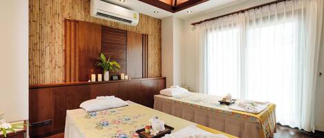 A hotel room with two beds, a wooden wall panel, an air conditioning unit, and a large window with sheer curtains.
