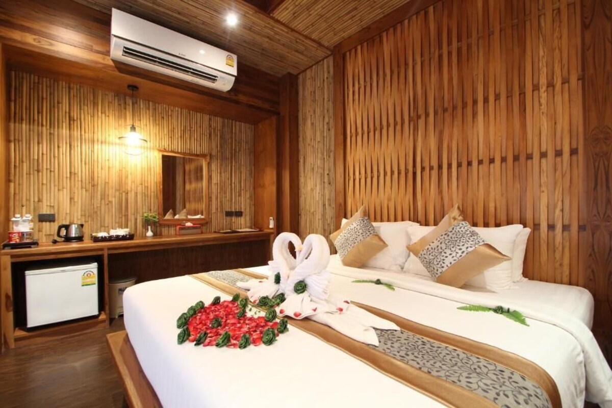 A hotel room with a wooden interior, a bed with white bedding, a small desk with a refrigerator, and a wall-mounted air conditioner.