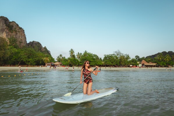 A person paddleboarding on a calm body of water with a beach and palm trees in the background. - Railay Village Resort & Spa (Krabi)