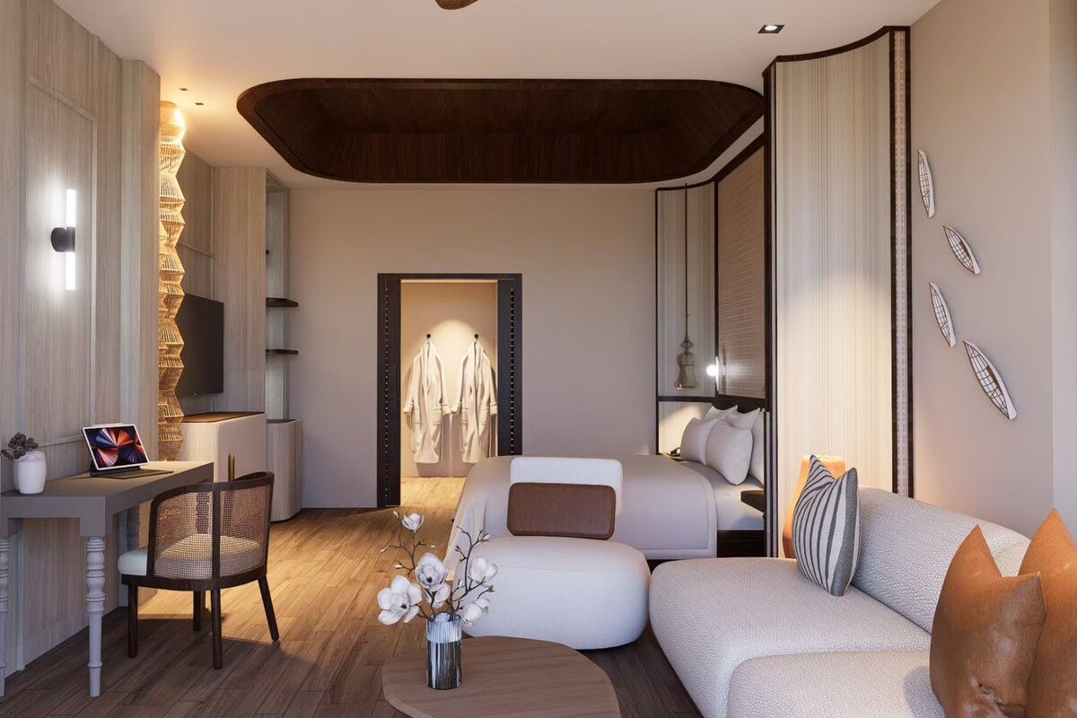 A modern hotel room with a sofa, a desk with a laptop, a chair, and a bed with pillows.