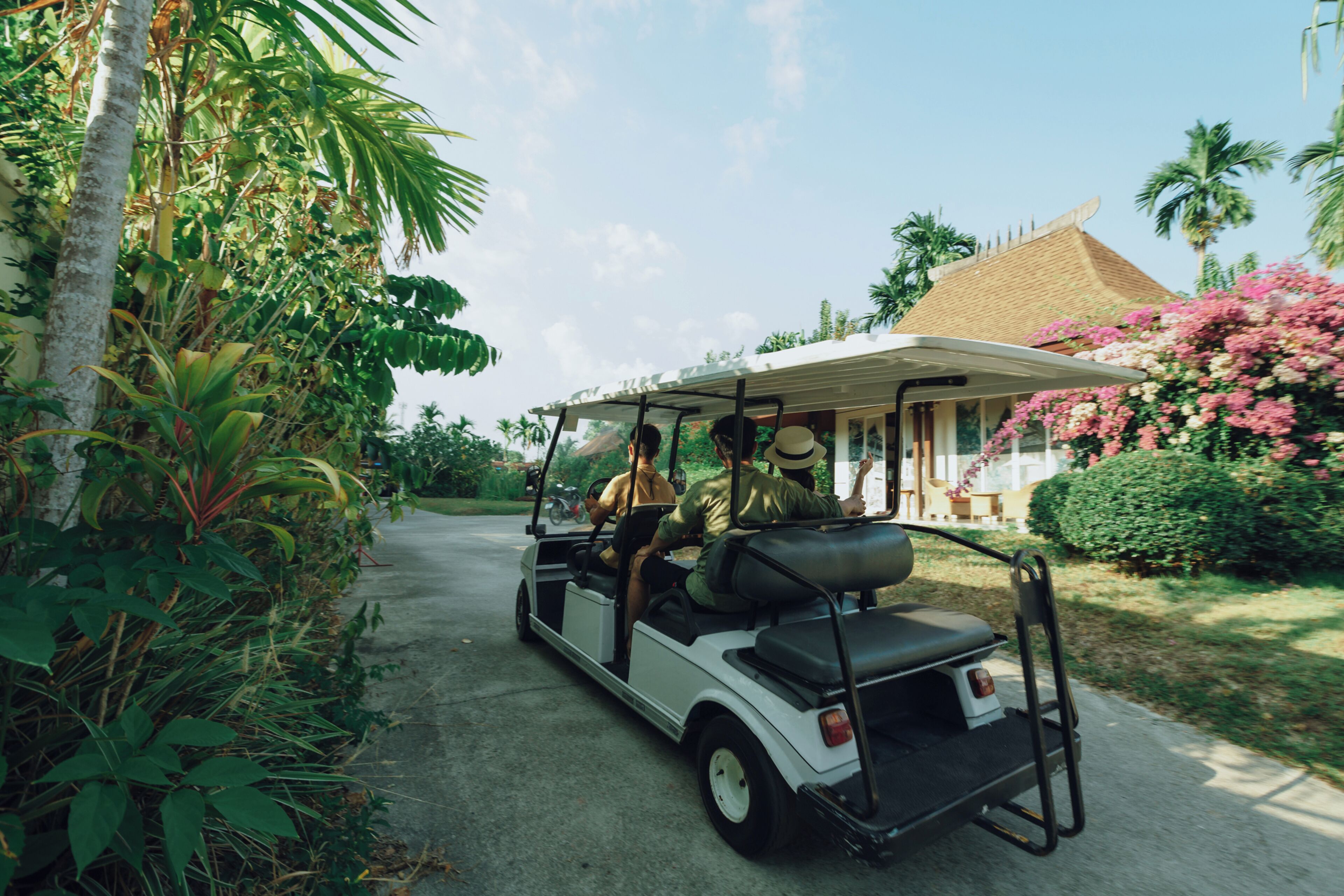 A golf cart parked on a driveway with lush greenery and a house in the background.