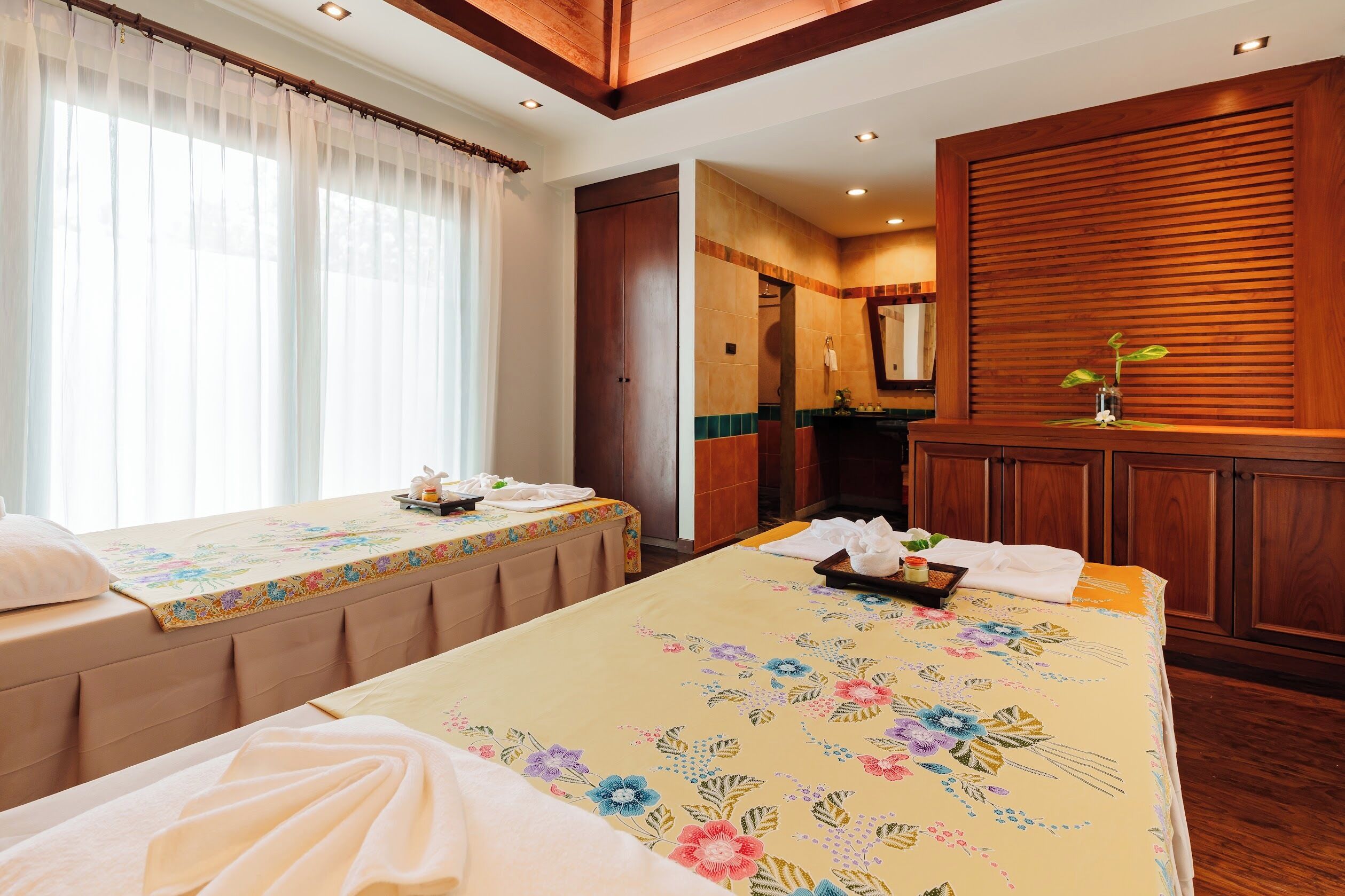 A hotel room with two beds, a wooden cabinet, a mirror, and a bathroom visible through an open door.