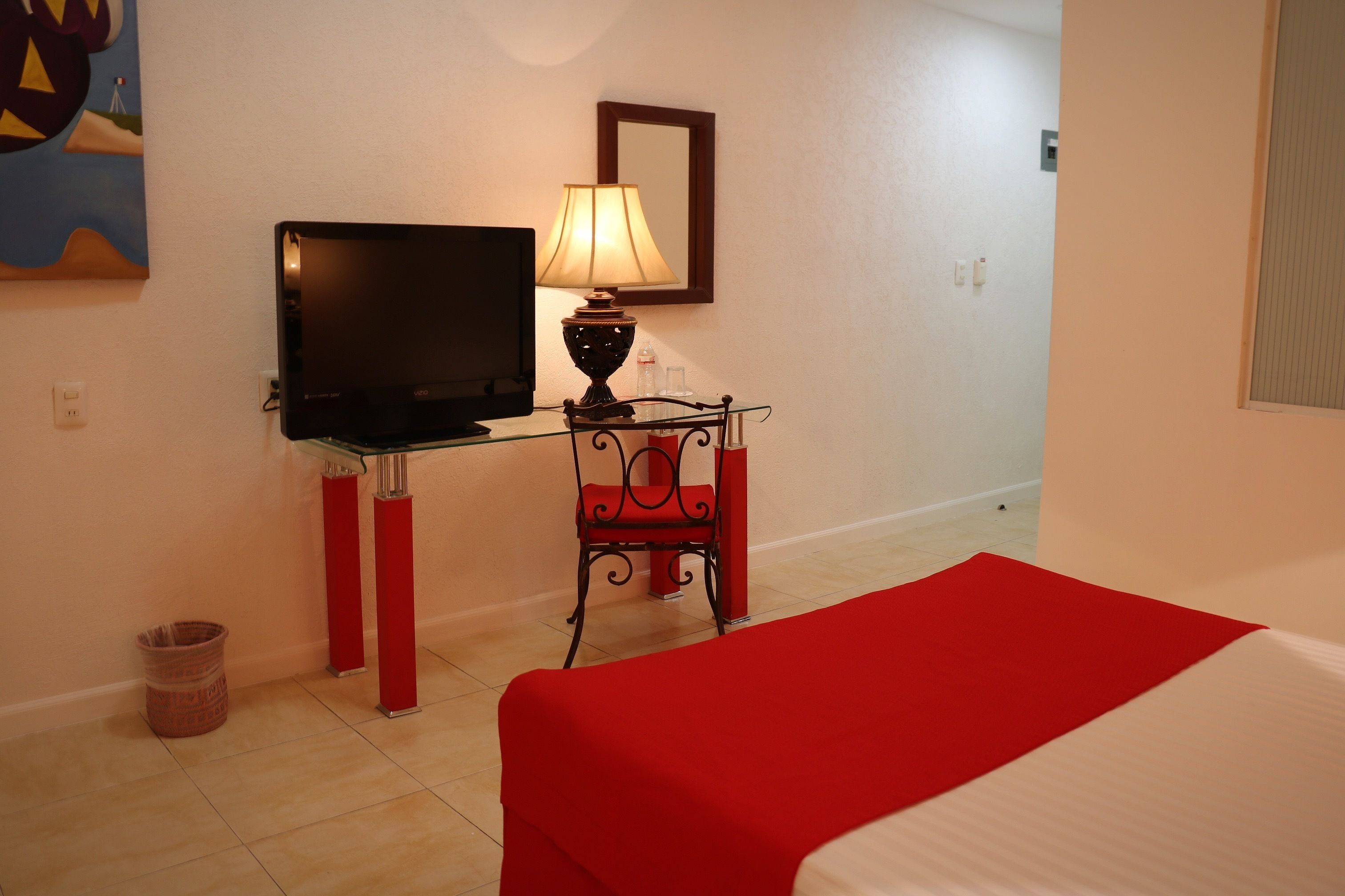 A hotel room with a bed, a TV, a desk with a lamp, and a chair.