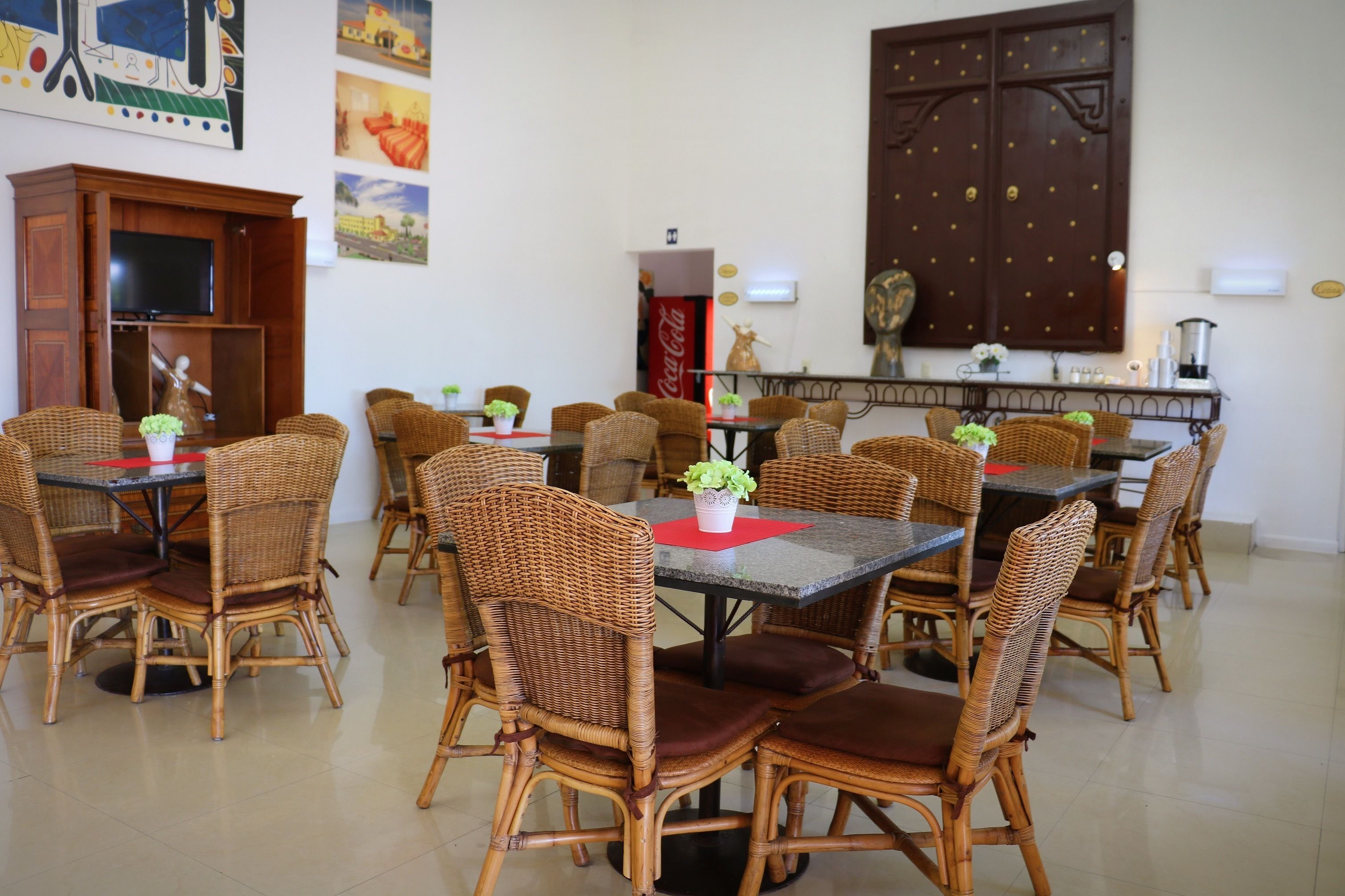 A dining area with wicker chairs and tables, a television, and artwork on the walls.