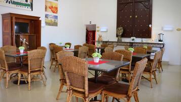 A dining area with wicker chairs and tables, a television, and artwork on the walls.