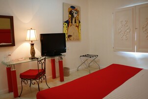 Habitación de hotel con cama, televisión, escritorio con lámpara, una silla y alfombra roja.