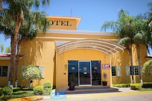 Fachada de hotel amarilla, con un amplio acceso en arco y palmeras.