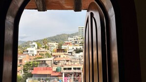Vista a través de un arco hacia un balcón con vistas a una zona urbana densamente poblada, con edificios y colinas al fondo.