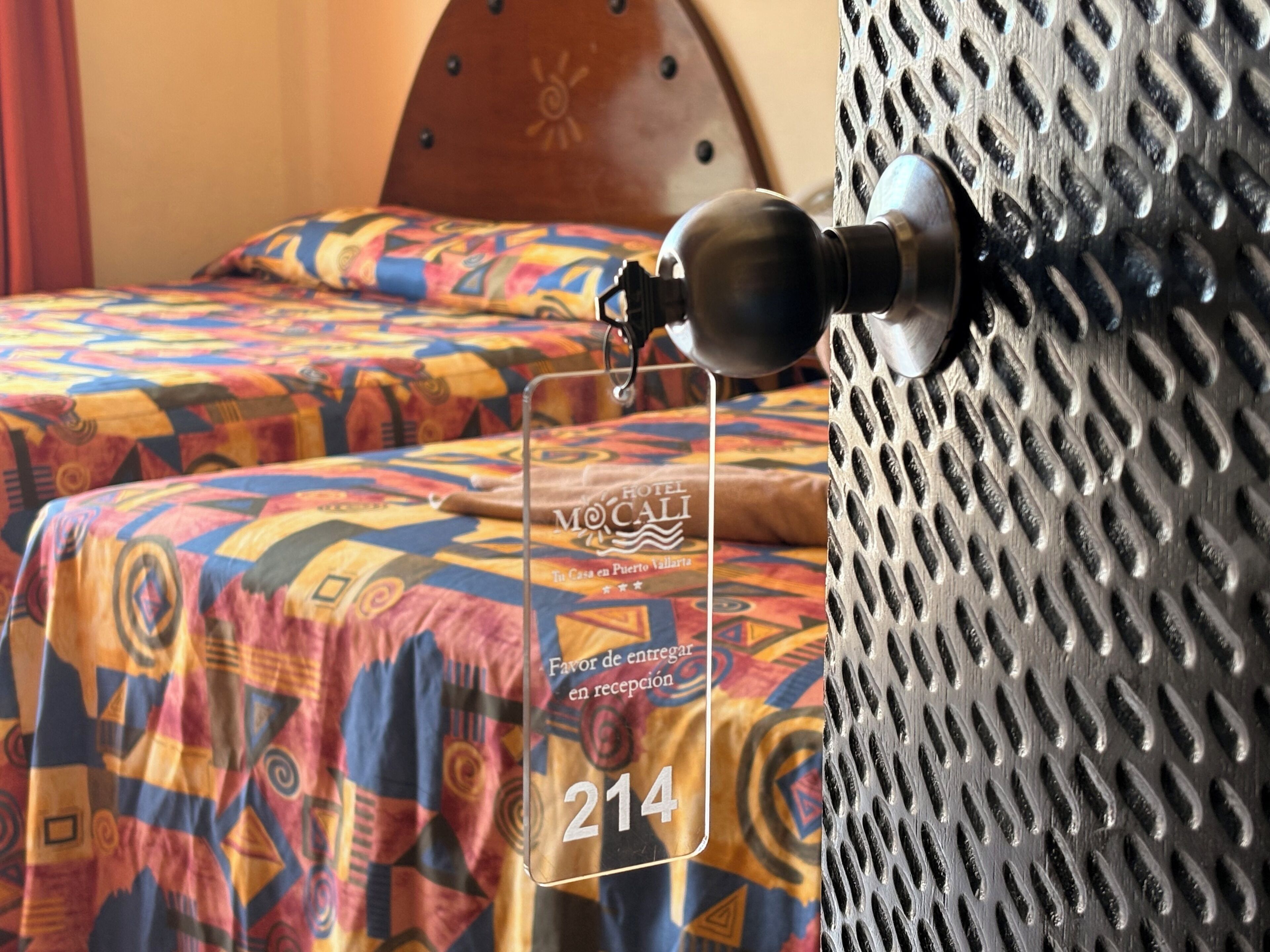 Quarto de hotel com cama, travesseiro, luminária fixada na parede e parede texturizada.