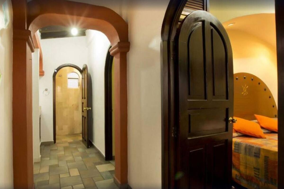 Un couloir avec une porte qui donne sur une pièce contenant un lit et des coussins orange.