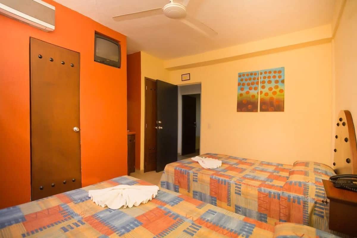 A hotel room with two beds, a ceiling fan, an air conditioning unit, a door, and a wall with a colorful artwork.