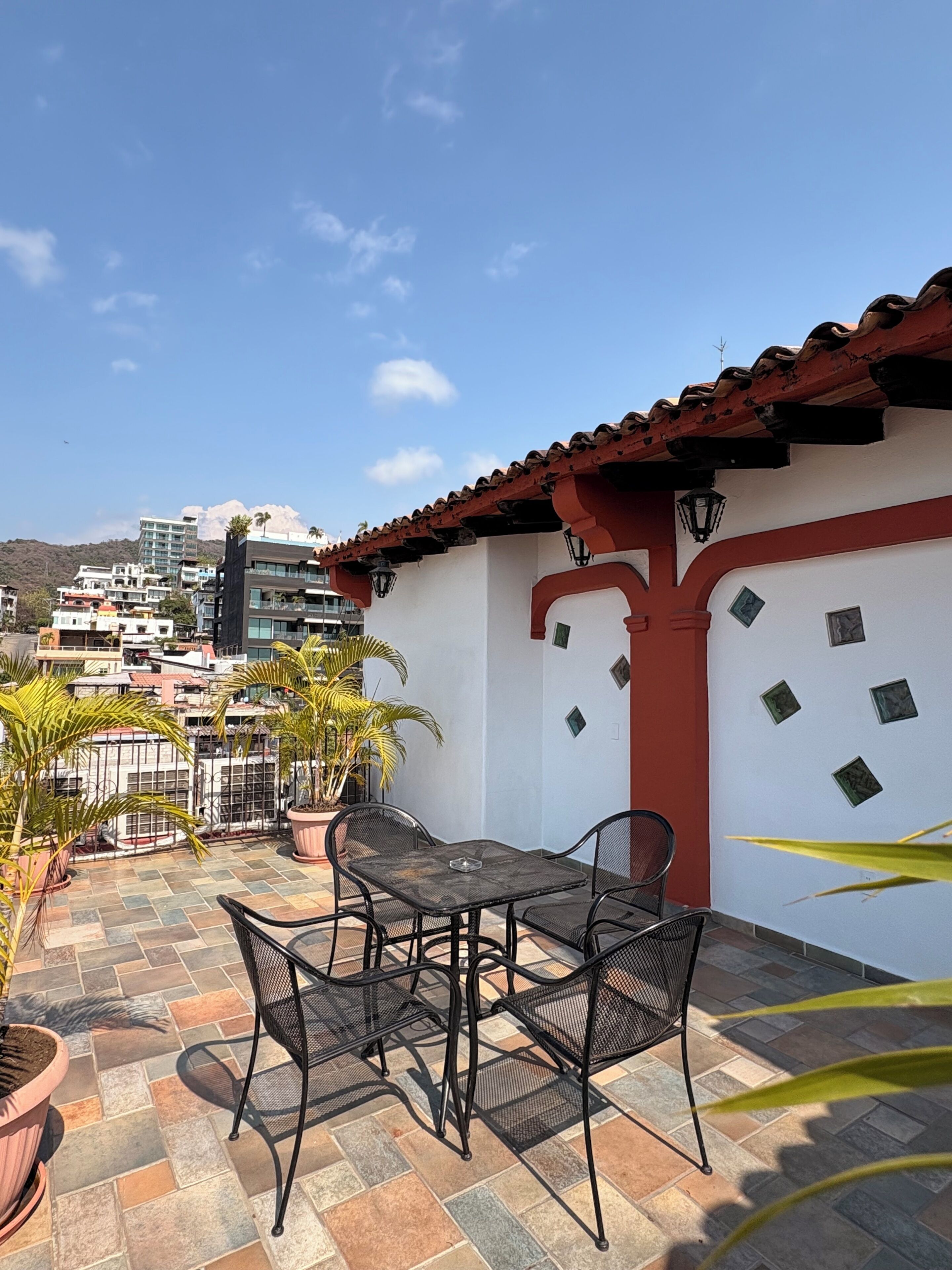 A patio with a table and chairs, potted plants, and a view of buildings in the background.