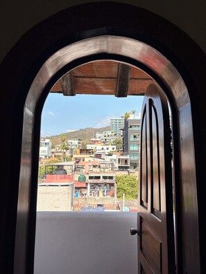 A view through an arched doorway of a cityscape with buildings and a hill in the background. - Hotel Mocali (Puerto Vallarta)