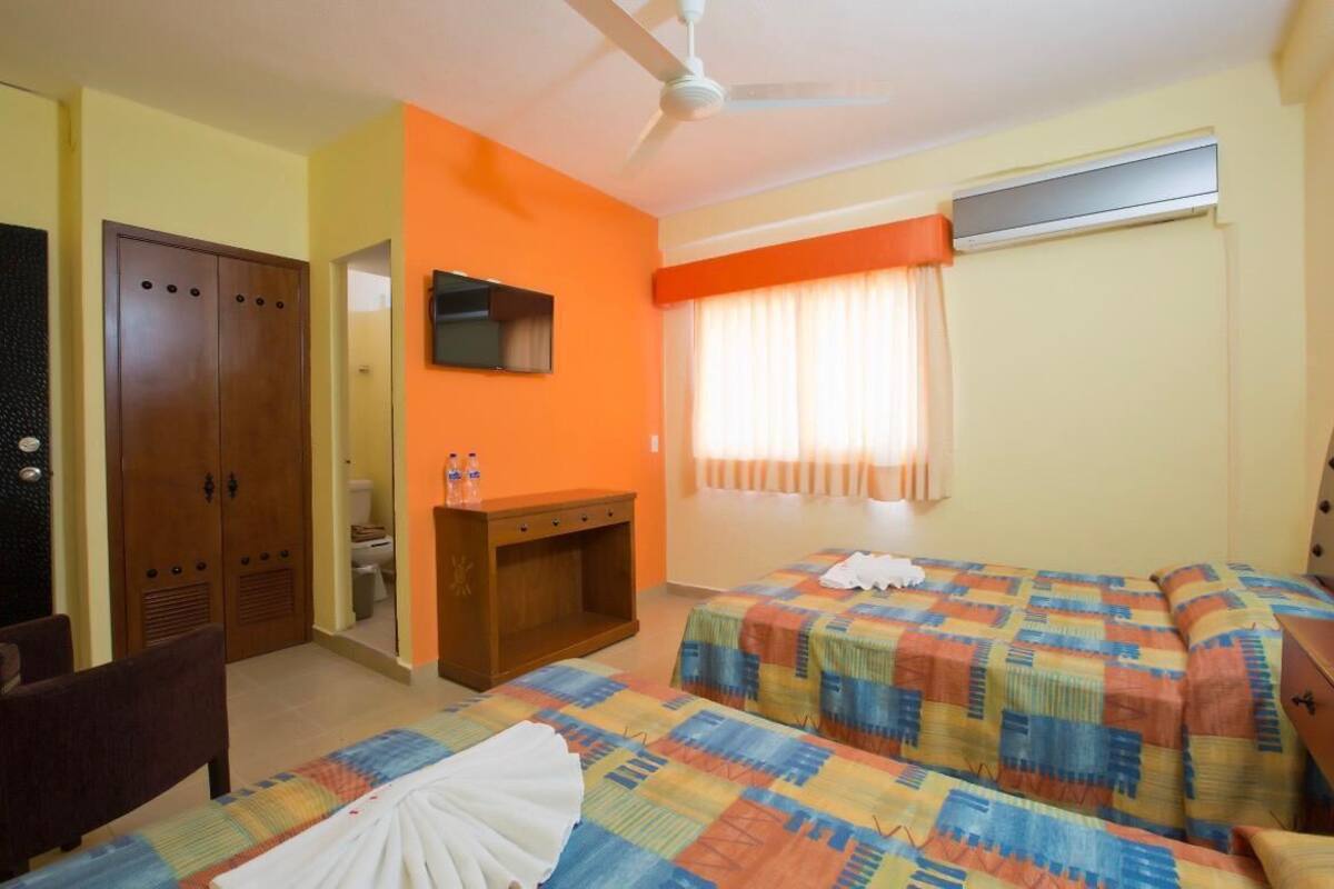 Une chambre d’hôtel avec deux lits, une armoire, un bureau, un ventilateur de plafond et une fenêtre avec des rideaux.