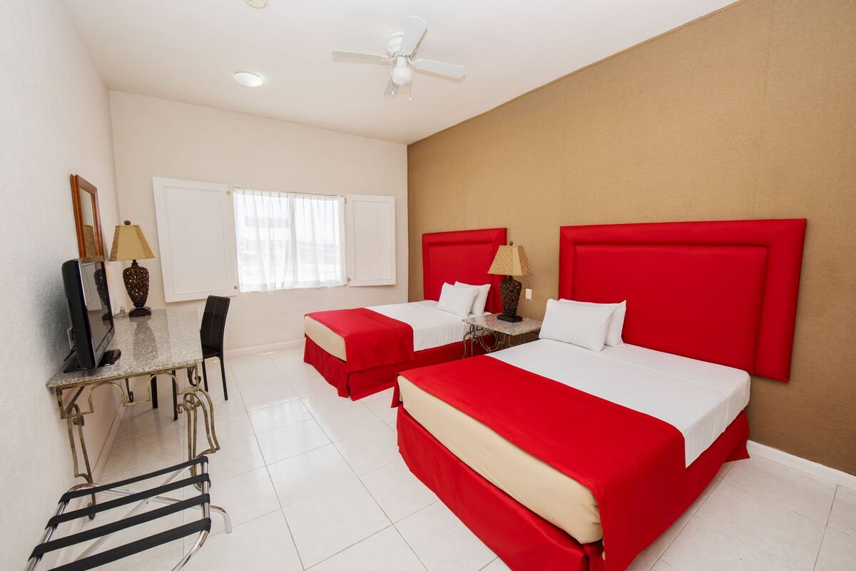 Une chambre d’hôtel avec deux lits, un bureau, une chaise, une télévision et un ventilateur de plafond.