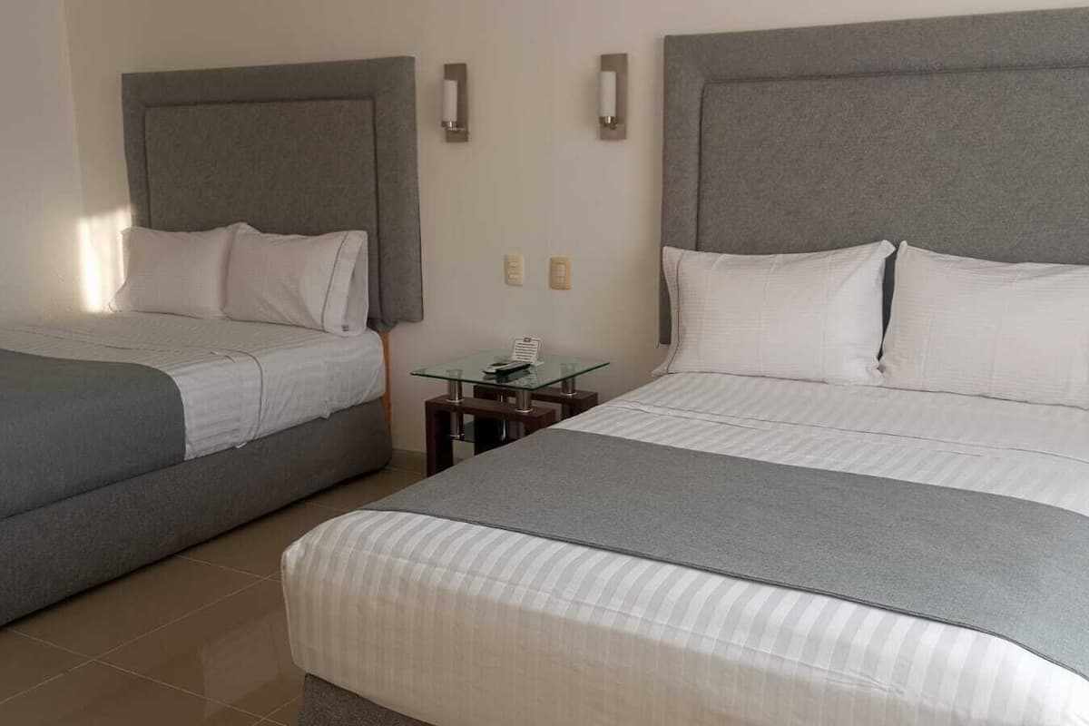 Une chambre d’hôtel avec deux lits, chacun doté d’une tête de lit grise et de linge de lit blanc. Une petite table avec un plateau en verre se trouve entre les deux lits.