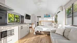 Une cuisine moderne équipée d’un four à micro-ondes, un coin repas avec une chaise, un lit avec une tête de lit et une grande fenêtre.