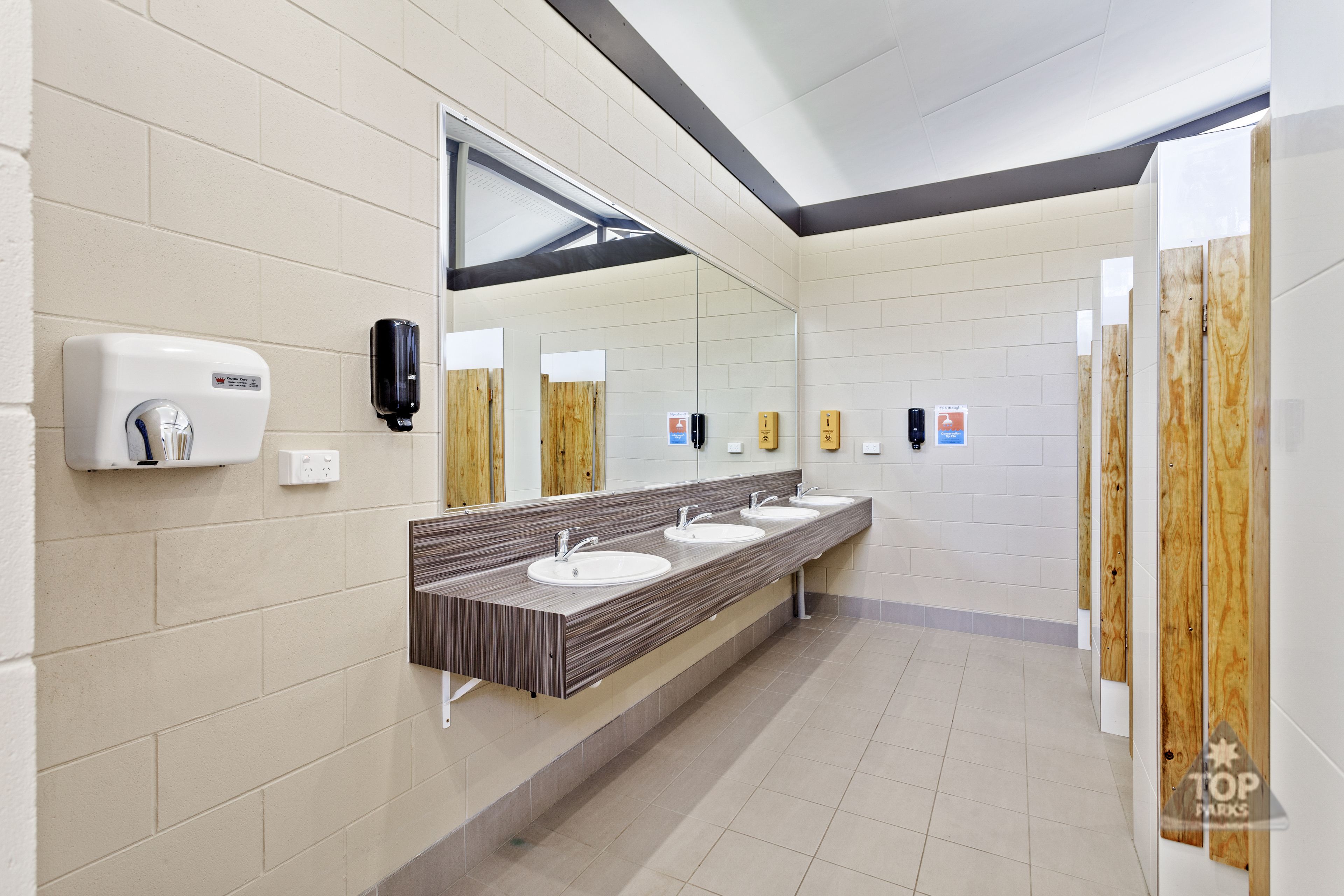 A public restroom with three sinks, a hand sanitizer dispenser, and wooden privacy partitions.