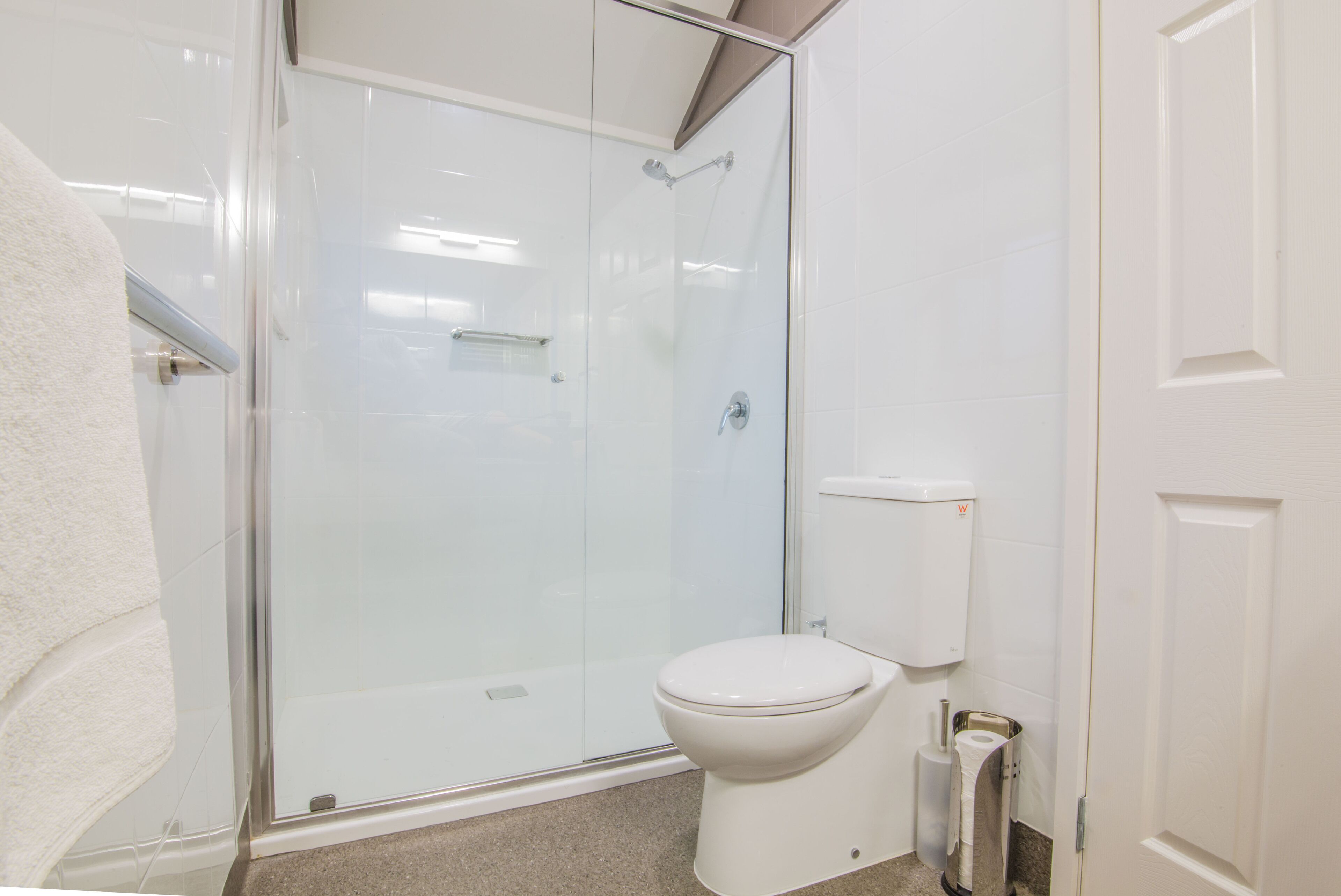 Un baño con ducha envuelta en vidrio, un inodoro blanco y un perchero.