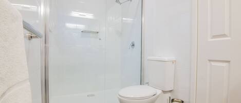 Un baño con ducha envuelta en vidrio, un inodoro blanco y un perchero.