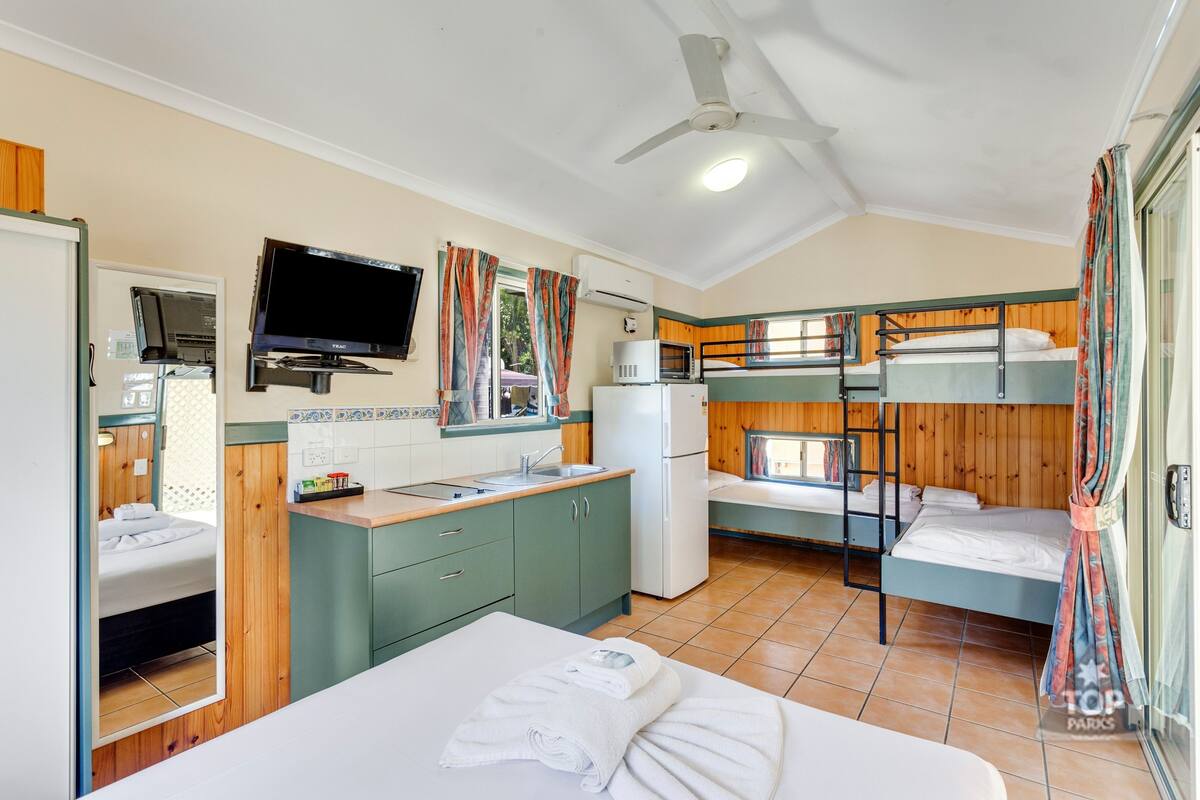 Une petite chambre avec des lits superposés, un coin cuisine, une télévision et un ventilateur de plafond.