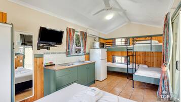 Habitación compacta con literas, kitchenette, televisión y ventilador de techo.