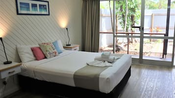 Una cama bien hecha con almohadas, una lámpara de noche y una ventana con cortinas.
