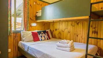 Dormitorio con literas, paredes de madera, una ventana con cortinas y una cama con almohadas y una toalla doblada.