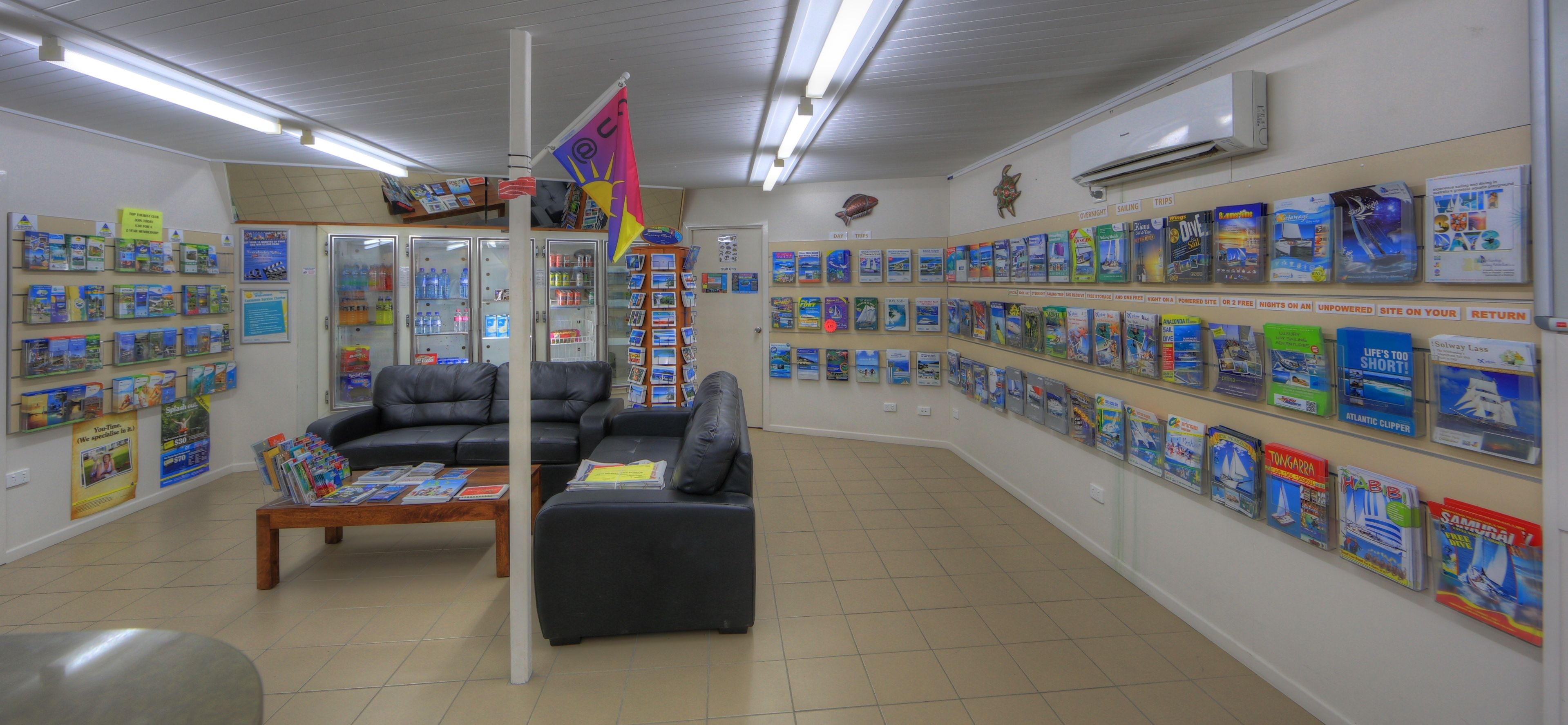A bookstore with a variety of travel books on display, a black leather couch, and a wooden coffee table.