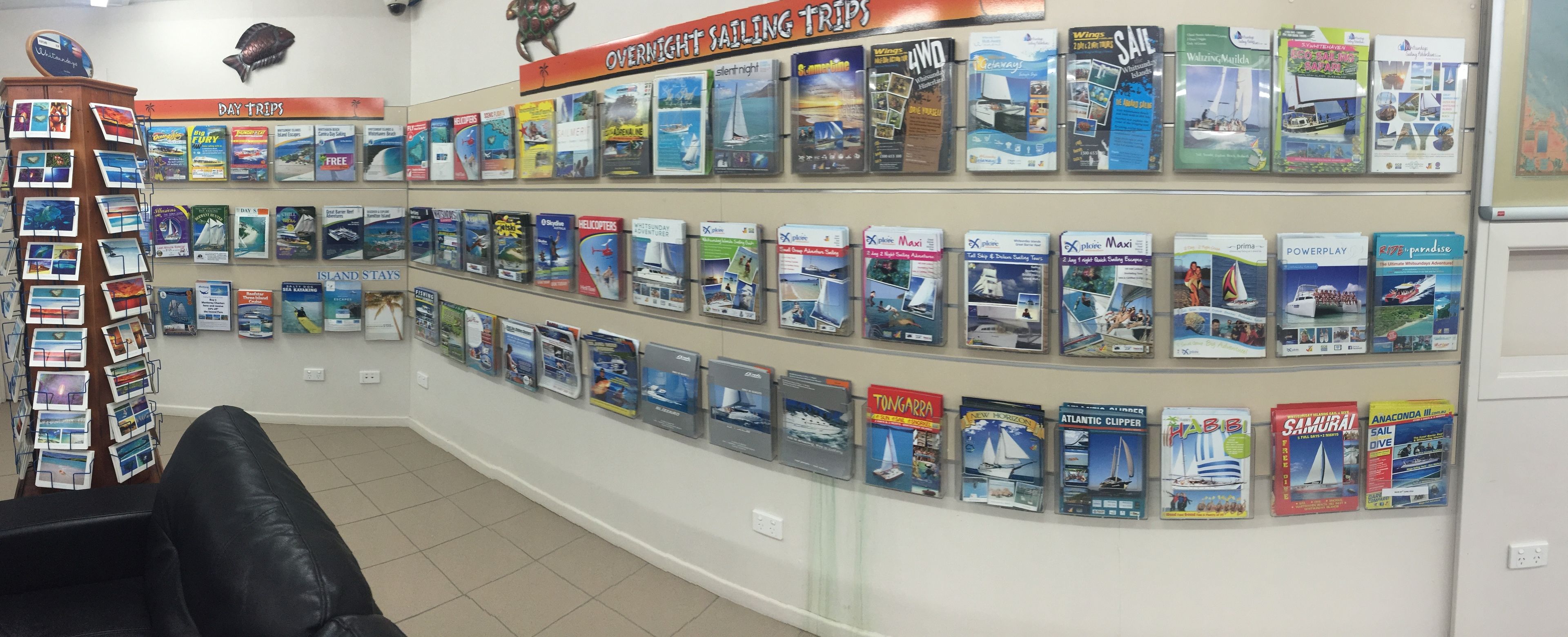 A travel agency wall with brochures for various trips, including sailing and island stays.