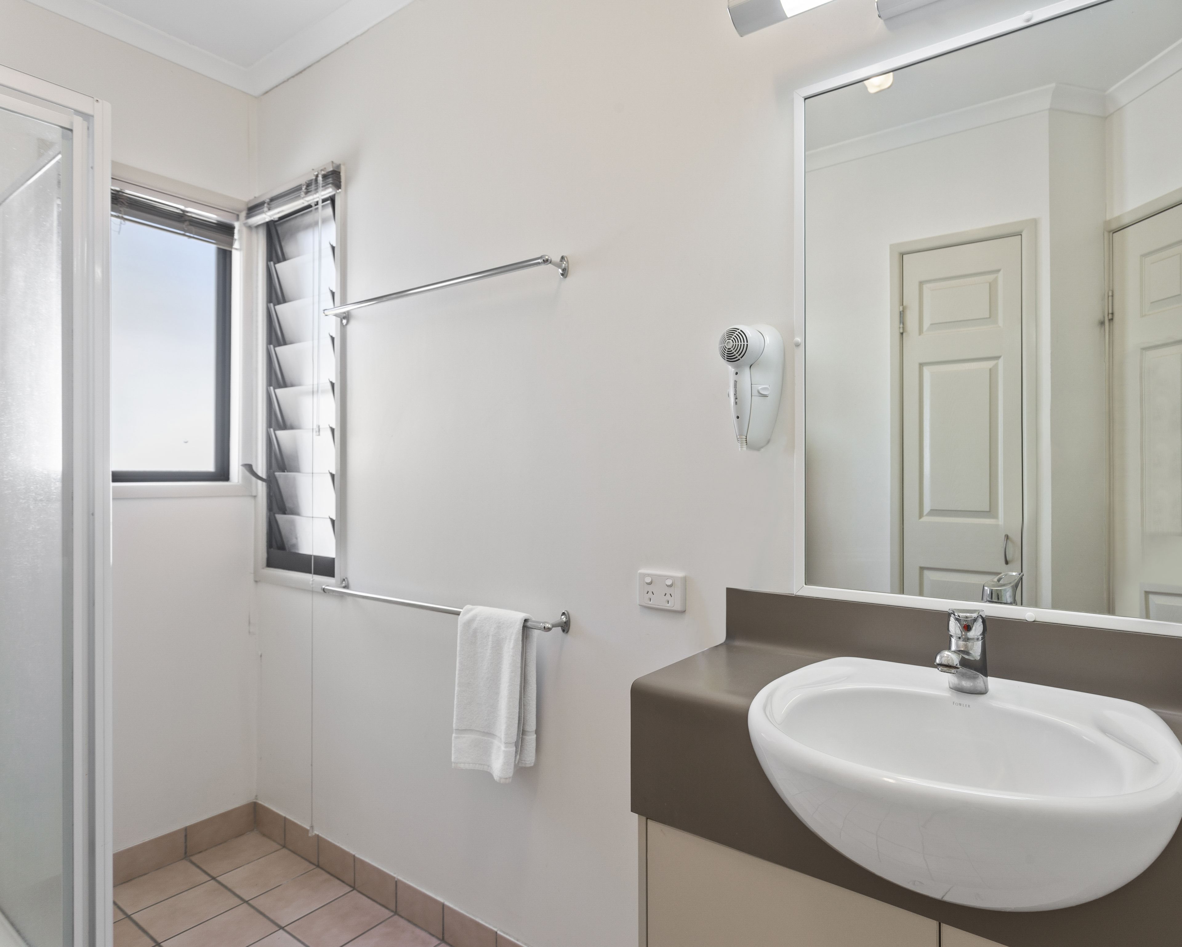 Ein Badezimmer mit einem weißen Waschbecken, einem Handtuchhalter, einem Fön und einem Fenster mit Jalousien.