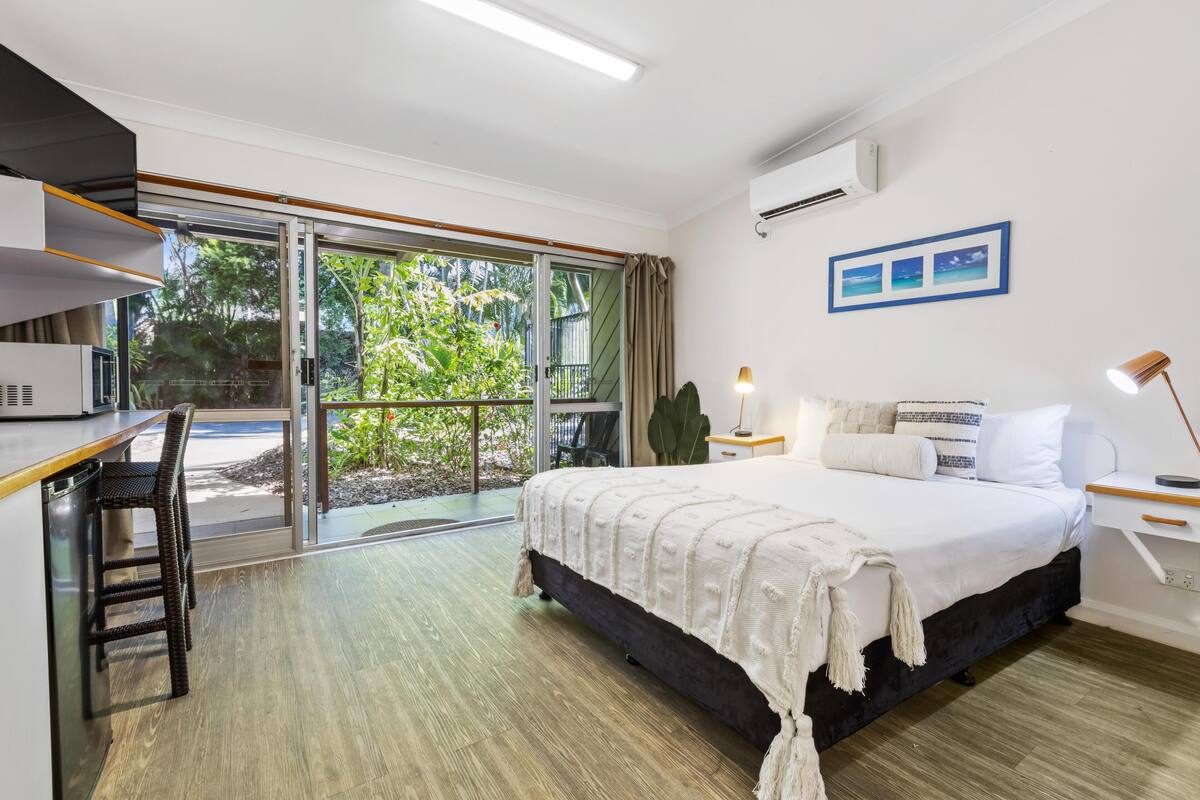 Une chambre d’hôtel moderne dotée d’un grand lit, d’un bureau et d’une porte-fenêtre coulissante donnant sur l’extérieur.