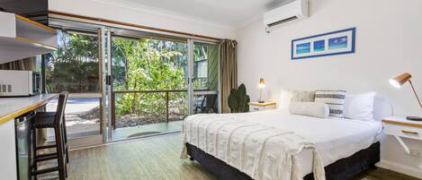A modern hotel room with a large bed, a desk, and a sliding glass door to the outdoors.