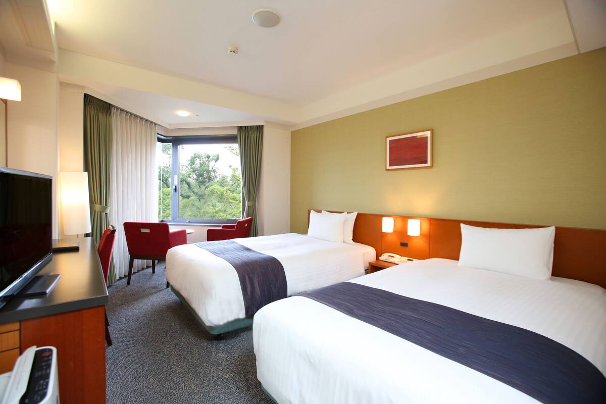 Habitación de hotel con dos camas, un escritorio, un televisor, una silla y una ventana con cortinas.