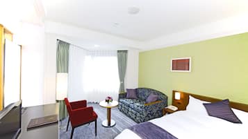 A hotel room with a bed, a sofa, a desk with a computer, and a small table with a vase of flowers.