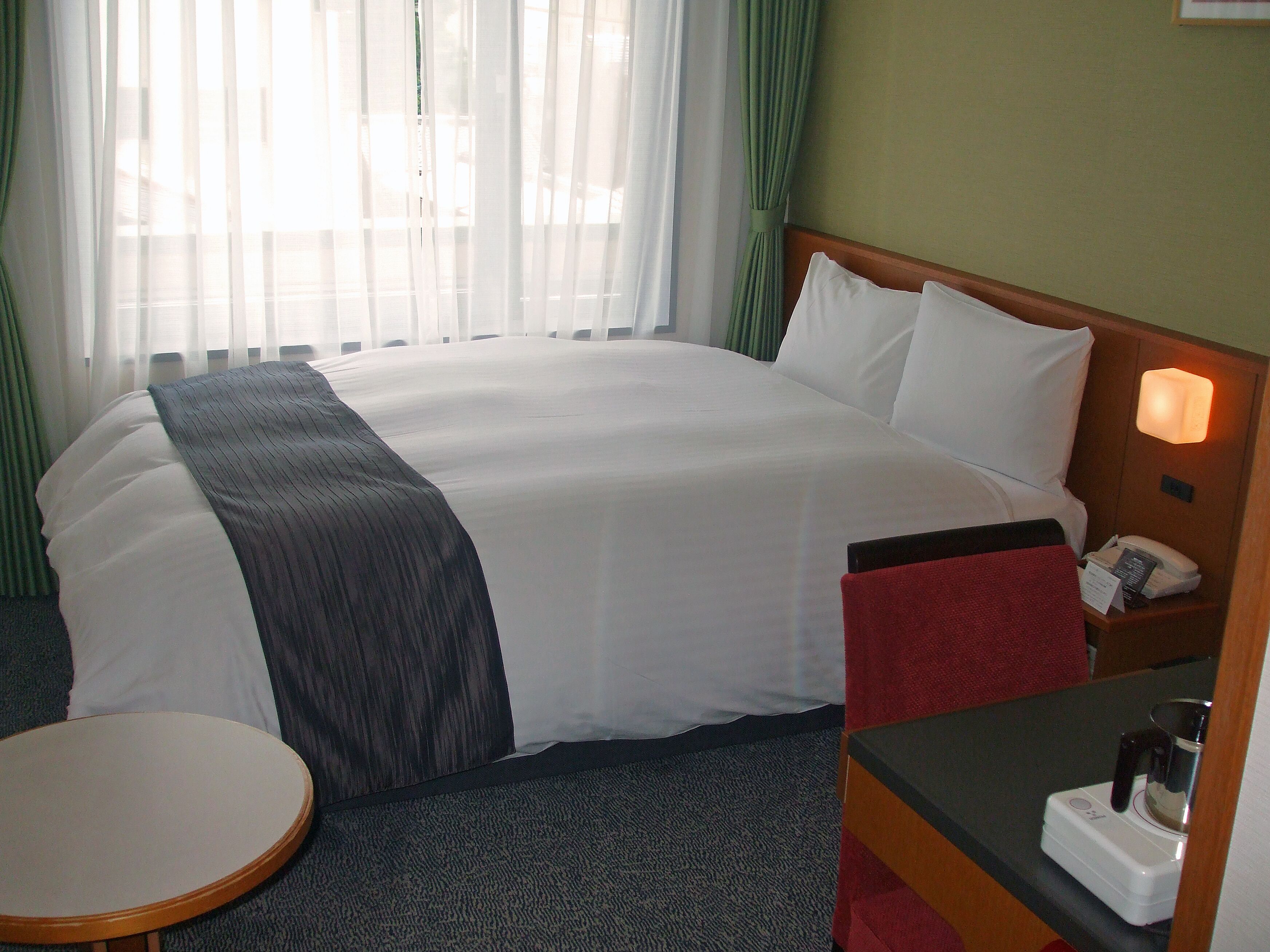 A hotel room with a large bed, a bedside table with a lamp, and a small round table.