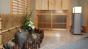 A traditional Japanese interior with tatami flooring, a bamboo fence, a stone water feature, and a sliding door with a hanging scroll. - Kyoto Garden Palace (Kyoto)