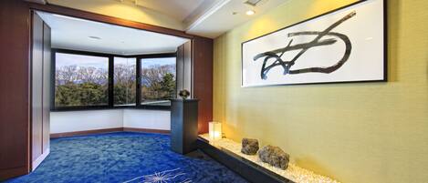 A hotel lobby with a blue carpet, a large abstract painting, a small water feature, and a view of trees through large windows.