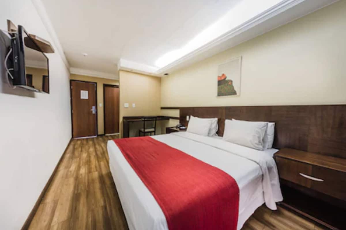 Una habitación de hotel con una cama grande, suelo de madera, escritorio y espejo.