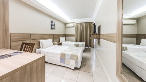 Een hotelkamer met twee bedden, een houten hoofdeinde, een bureau en een spiegel.