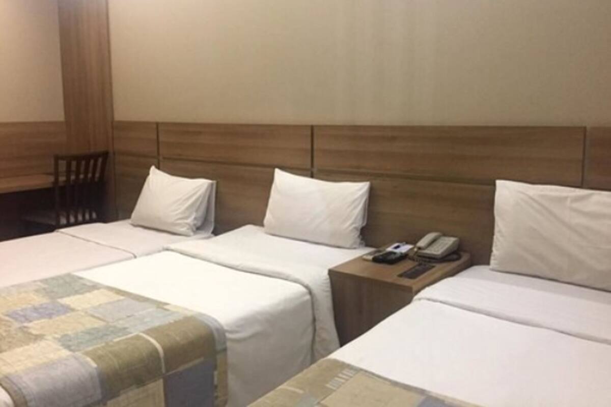 Habitación de hotel con dos camas, cabecera de madera, una mesita con teléfono y una silla.